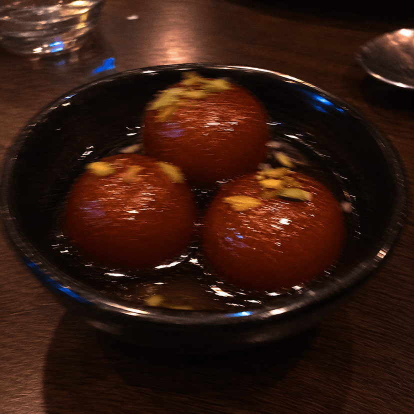 A blurry low-light photo of gulab jamun taken quickly on a phone.