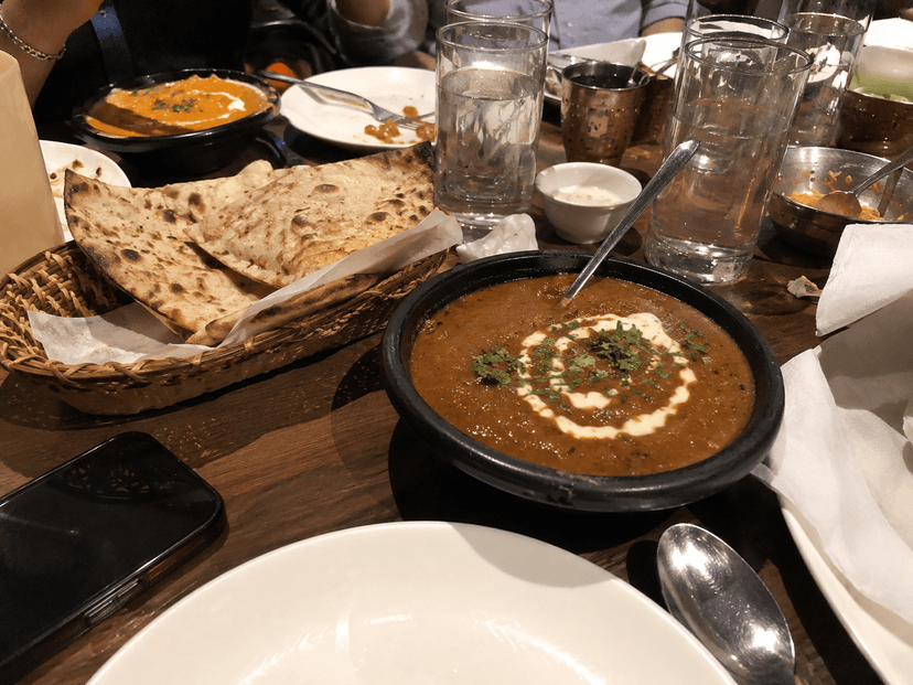 Dal makhani on a cluttered restaurant table with glasses, plates, and other objects visible.
